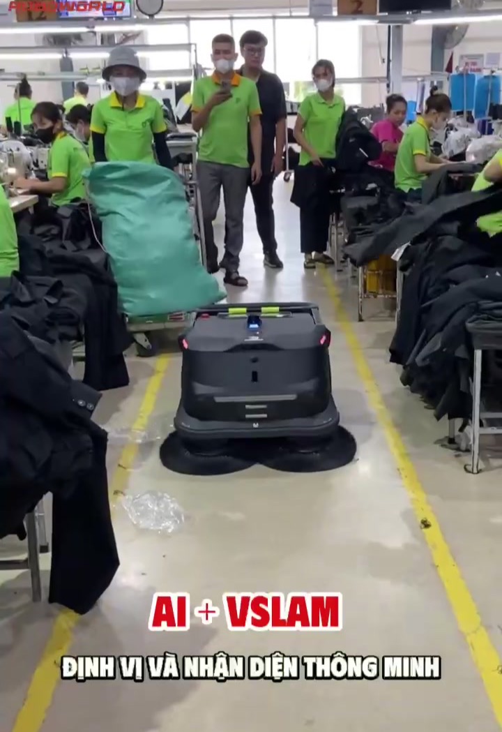 Robot PUDU MT1 tự chạy quét — hút bụi giữa các chuyền may, né người và máy móc, không làm gián đoạn sản xuất (ảnh thật tại nhà máy khách hàng Roboworld).